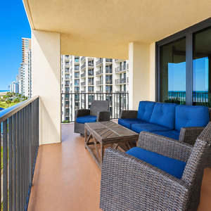 Balcony features wicker seating with blue cushions, offering views of the beach and nearby pool area