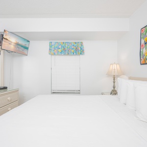Inviting bedroom featuring a king bed, colorful artwork, and a wall-mounted TV for entertainment