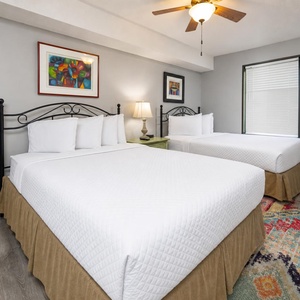 This guest bedroom features two queen beds complemented by colorful artwork and a cozy area rug
