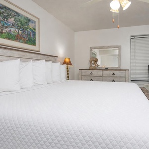 Serene bedroom features a large king bed, a stylish dresser, and a TV, complemented by colorful artwork and soft lighting