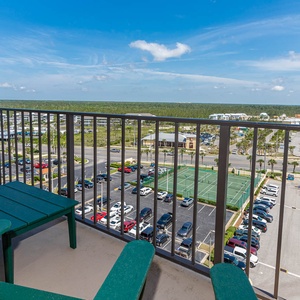 A green adirondack chair overlooks a vibrant parking lot and tennis courts on the master balcony, framed by a clear blue sky