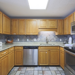 Warm wooden cabinetry complements the spacious counter, featuring stainless appliances, and a coffee maker