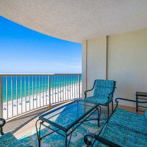 The balcony features comfortable seating with tropical-patterned cushions and offers a stunning beachfront view