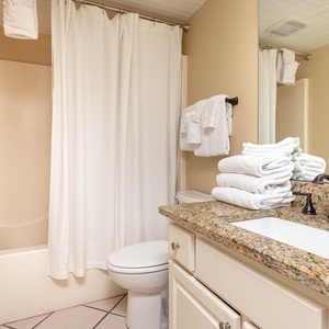 The guest bathroom features a granite countertop, neatly stacked towels, and a tub/shower combo with a white curtain