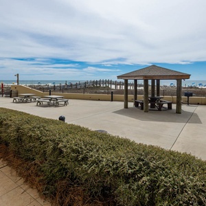 Outdoor patio area features a shaded gazebo, picnic tables, and a view of the beach with colorful umbrellas in the distance