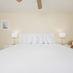 Master bedroom features a large king bed with plush pillows, complemented by modern lamps and coastal artwork on the walls
