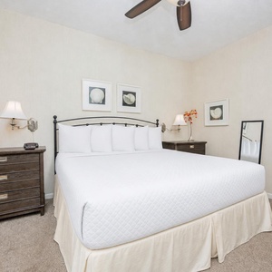 Bright bedroom featuring a king bed with plush white linens, stylish nightstands, and decorative art
