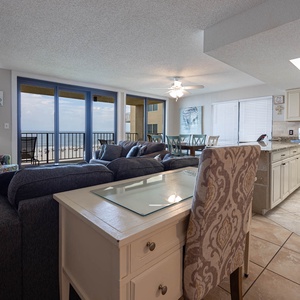 The living area features a sectional sofa with queen sleeper, a flat-screen TV, and breathtaking beach views from the balcony