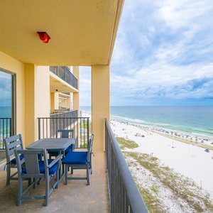 The balcony features a table with red and blue chairs, offering a direct view of the beach and turquoise waters below