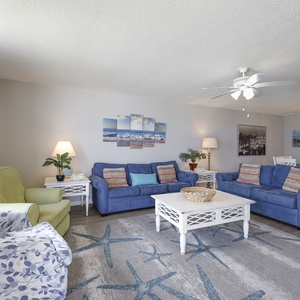 The living area features vibrant blue sofas with queen sleeper, a cozy green chair, and beach decor, for a welcoming vibe