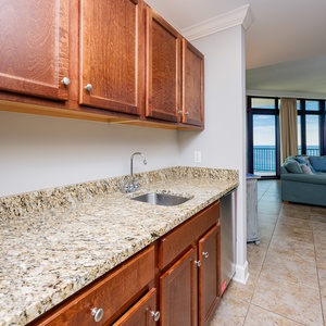 This wet bar features rich wood cabinetry, a granite countertop, blender, and a view of the beachfront through large windows
