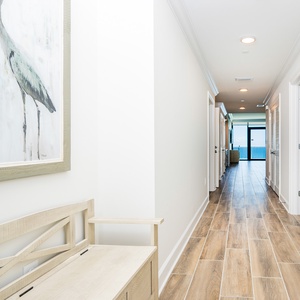 Step into a welcoming hallway featuring a decorative bench and artwork, leading to a stunning beach view
