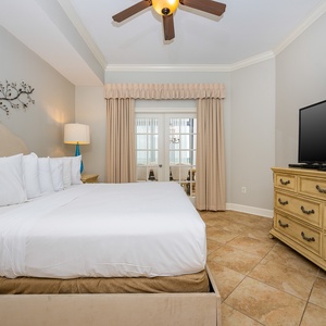 The master bedroom features a plush king bed, a large TV, and elegant decor, with natural light from the dining area