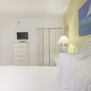 Brightly decorated guest bedroom featuring a queen bed, a flat-screen TV, and a charming lamp beside a colorful painting
