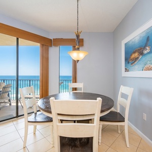 Bright dining area featuring a round table with four chairs and panoramic views of the beach