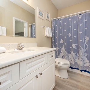 The bathroom features a white vanity with a stylish countertop, a decorative blue shower curtain, and elegant coastal decor