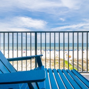 Relax in the comfortable chair while enjoying expansive views of the beach and vibrant blue skies from your balcony