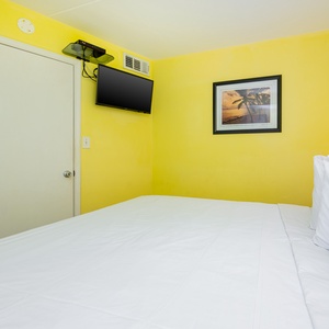 This bright room features a comfortable bed, a mounted TV, and cheerful yellow walls, perfect for a relaxing getaway