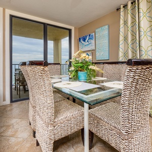 Natural light fills the dining room where your family gathers around the glass table with coastal views beyond the balcony