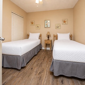 Inviting guest bedroom featuring two twin beds, warm decor, and charming coastal artwork