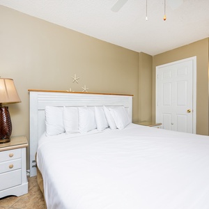 The master bedroom features a large bed with plush pillows, a stylish lamp, and a peek into a bright bathroom
