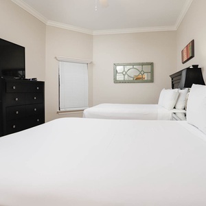 This guest bedroom features two comfortable queen beds, a wall-mounted TV, and stylish decor for a relaxing stay