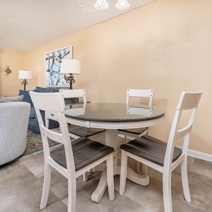 Bright dining area features a round glass-top table with white chairs, complemented by cozy seating and a view of the gulf