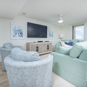 Cozy seating area features soft blue chairs and a large sofa with queen sleeper, with a TV and views of the beach