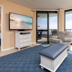 Cozy living area features a large TV, comfortable seating, and access to a balcony with a view of the beach