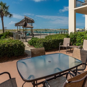 Outdoor seating area featuring a glass-top table and chairs, surrounded by lush greenery and a view of the pool area