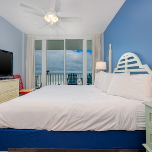 The master bedroom features a large bed, a TV, and a stunning beachfront view from the balcony, perfect for relaxation