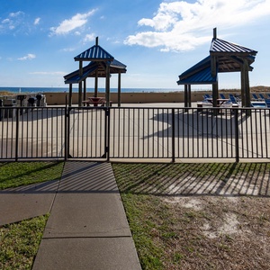The outdoor pool area features shaded pavilions, a pool, and a view of the beach, perfect for relaxation and gatherings