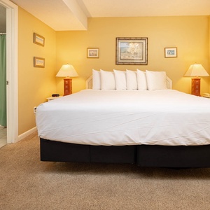 The master bedroom features a plush king bed with multiple pillows, warm yellow walls, and en-suite bathroom