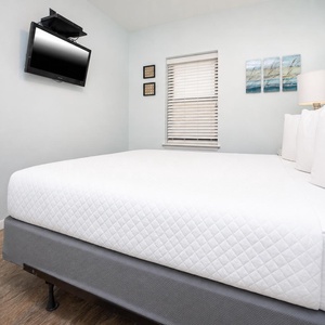 Guest bedroom featuring a queen bed, mounted TV, and soft blue walls, creating a serene retreat for relaxation