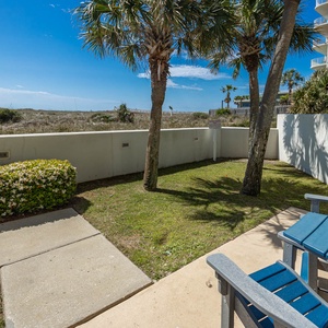 Seating in blue adirondack chairs overlooks a grassy area bordered by palm trees, creating a serene outdoor retreat