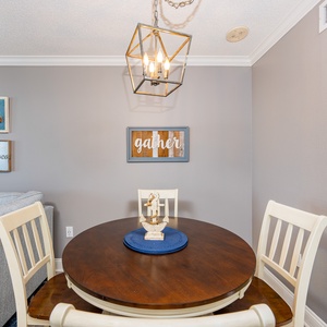 Cozy dining area features a round wooden table with a blue placemat, surrounded by white chairs and nautical decor