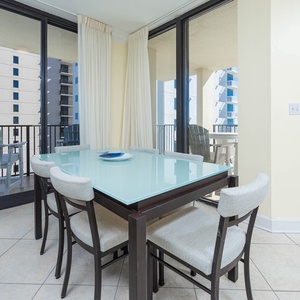 Dining area features a glass table with stylish chairs, offering a view of the balcony and the beach beyond