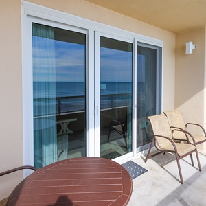Enjoy a beachfront view from this cozy balcony featuring a round table and two comfortable chairs, perfect for relaxation