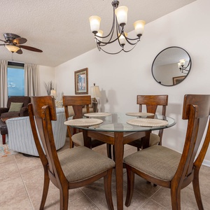 Dining area features a glass table with four wooden chairs, complemented by a cozy living space and a view of the beach