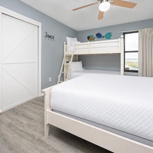 This guest bedroom features a queen bed, a charming twin bunk bed, and colorful fish decor, perfect for a family getaway