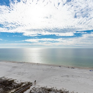 A serene view of the tranquil beach front with soft white sand and gentle waves under a bright blue sky filled with clouds