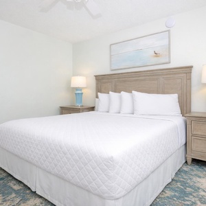 Spacious bedroom features a king bed, a decorative blue lamp, and soft area rug for added comfort