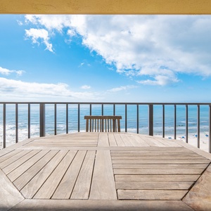 Balcony overlooks the tranquil beachfront, framed by a clear blue sky and gentle waves