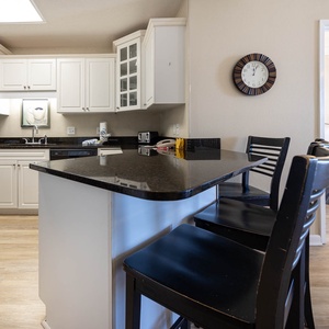 Bright kitchen features black countertops, white cabinetry, and a breakfast bar with seating, leading to the master suite