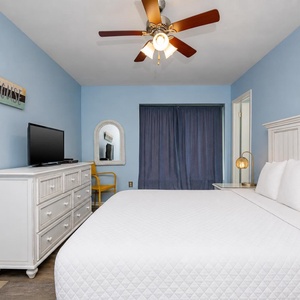 This bedroom features a comfortable bed, a TV for entertainment, and calming blue walls, creating a relaxing retreat