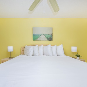 Master bedroom features a large king bed with numerous pillows, complemented by stylish bedside lamps and artwork