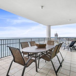 This expansive balcony features a dining table and lounge chairs, perfect for enjoying beachfront views and relaxation