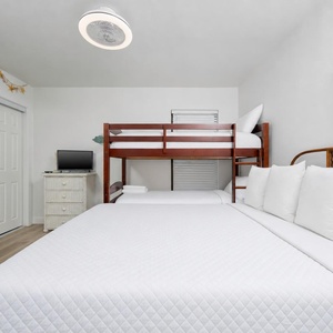 This cozy bedroom features a bunk bed and a queen bed, complemented by a TV and beach-themed decor for a relaxing stay