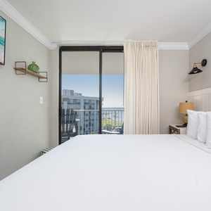 Cozy master bedroom featuring a king bed, wall-mounted TV, and a lovely view from the sliding glass balcony doors