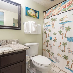 The guest bathroom features a playful animal-themed shower curtain, a stylish granite countertop, and a large mirror